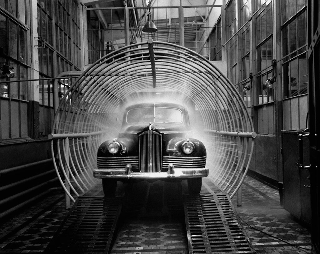 Historický automobil prechádza myčkou v továrenskej hale na testovanie vodotesnosti.