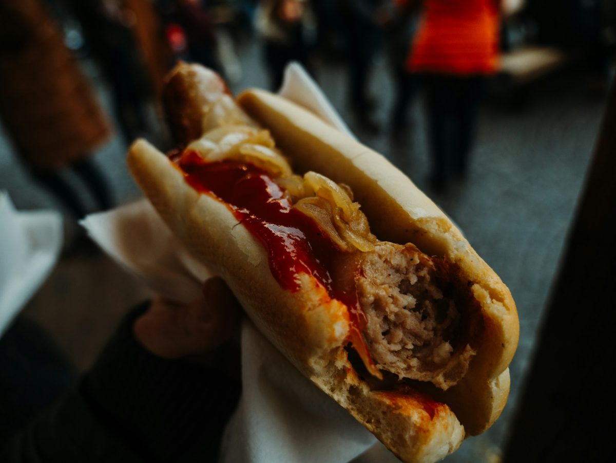 Hotdog s kečupom a cibuľou v žemli, držiaci v ruke na trhu.