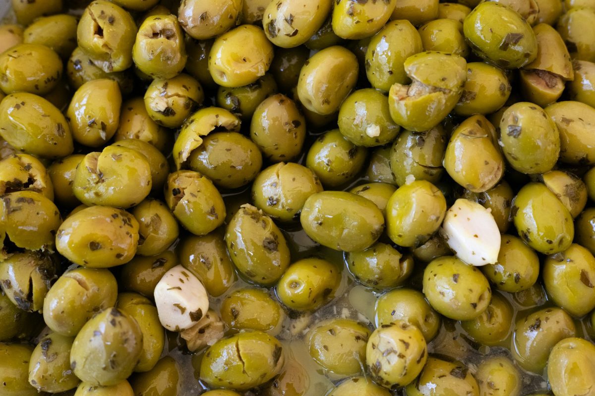 Zelené olivy a cesnak marinované v bylinkovej zmesi, detailný záber chutného predjedla.