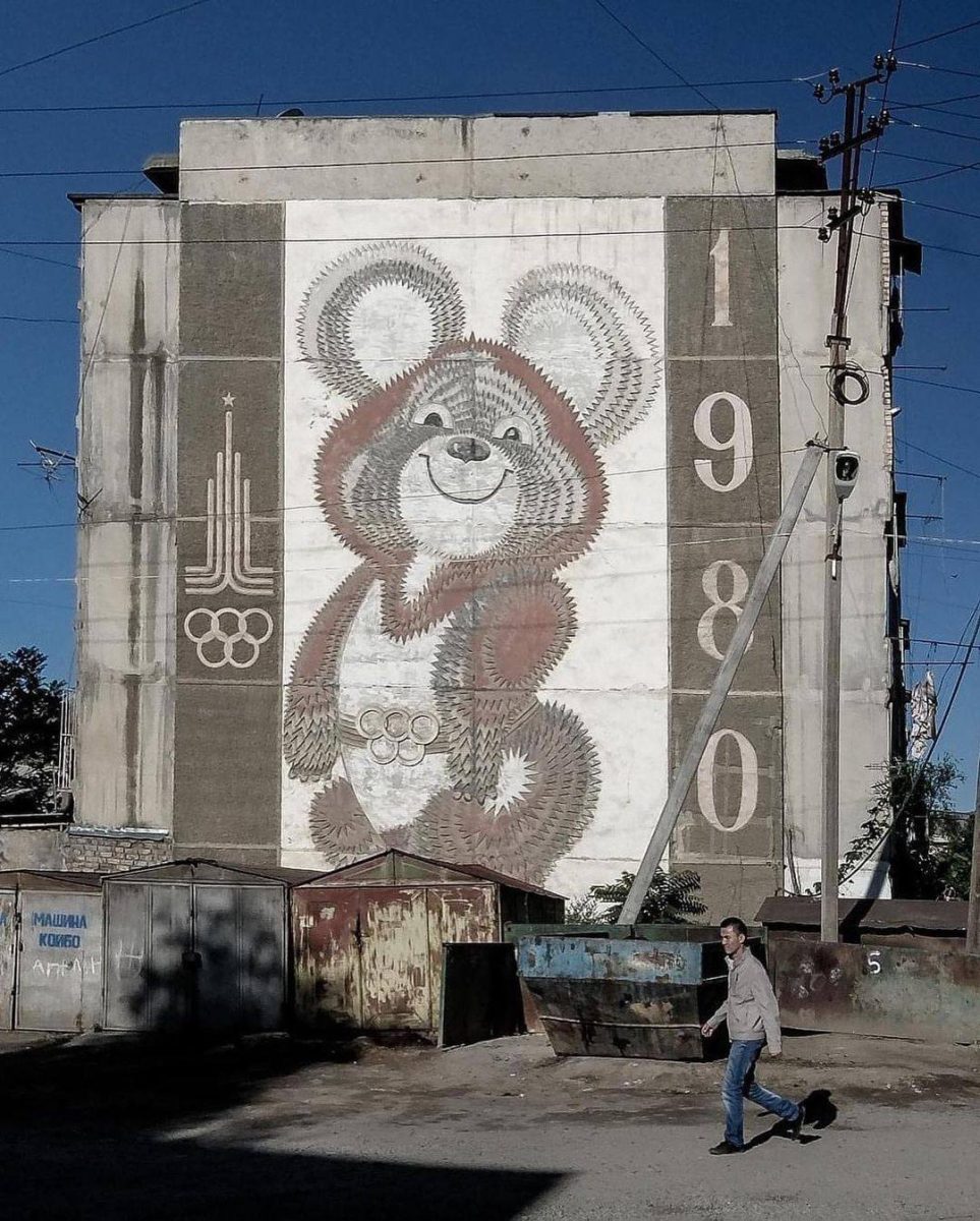 Mural medveďa z olympiády 1980 na stene budovy so zamračenou oblohou v pozadí.
