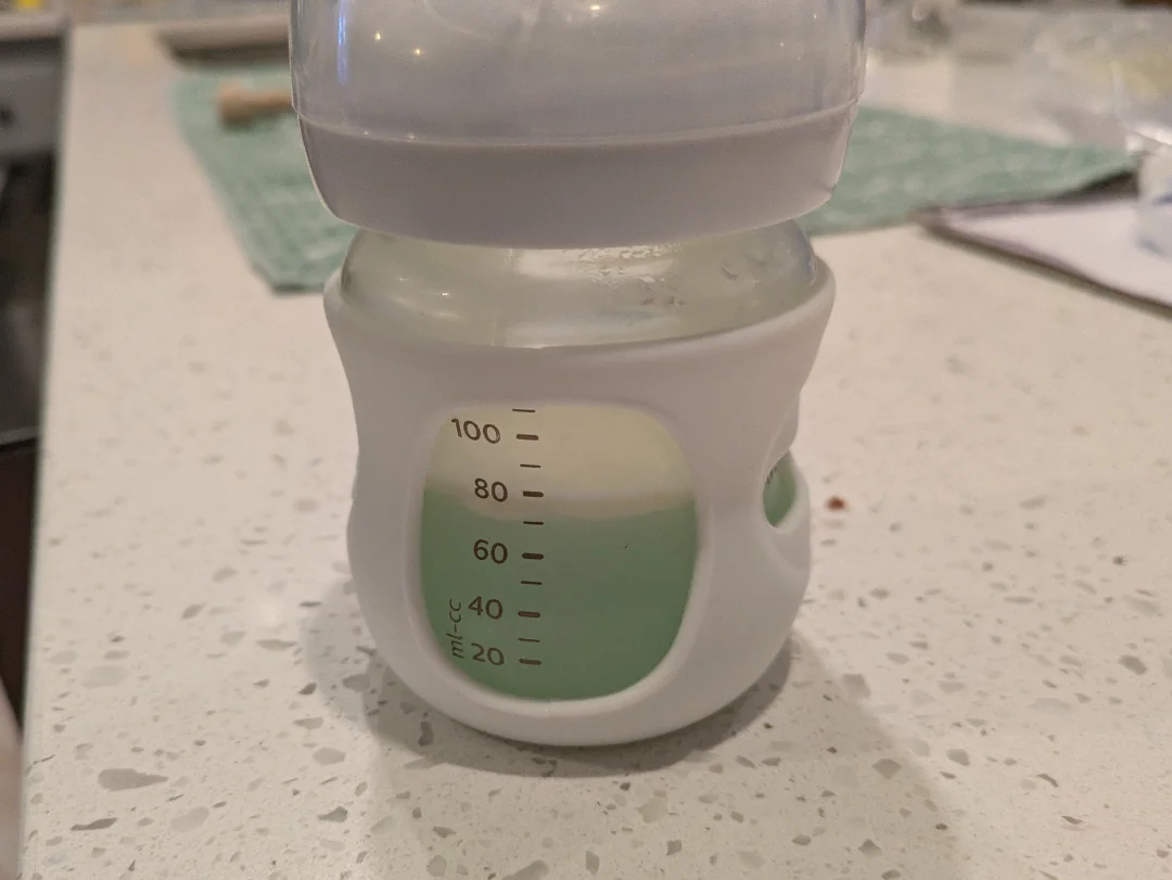 Detská fľaša s mliekom na kuchynskej doske s odmerkou do 100 ml.