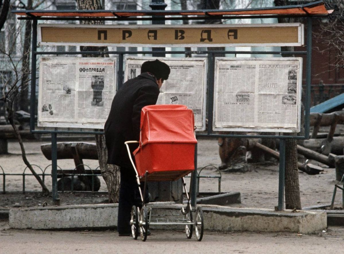 Muž s kočíkom číta nástenné noviny na ulici, zimná scéna so staromódnym kočíkom.