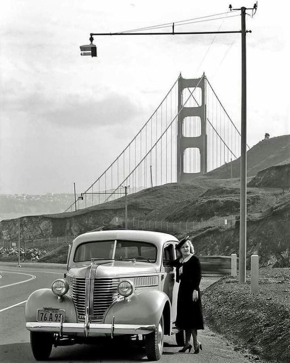 Žena s retro autom pri ikonickom moste Golden Gate v San Franciscu, historická čiernobiela fotografia.