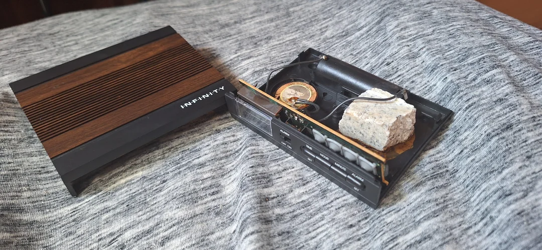 Starý rozobratý elektronický prístroj s viditeľným kameňom a vnútornými mechanizmami, položený na sivom podklade.