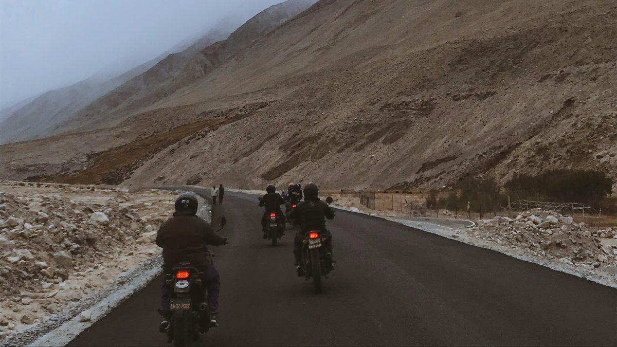 Motorkári na horskej ceste obklopeni skalnatou krajinou za zamračeného počasia.