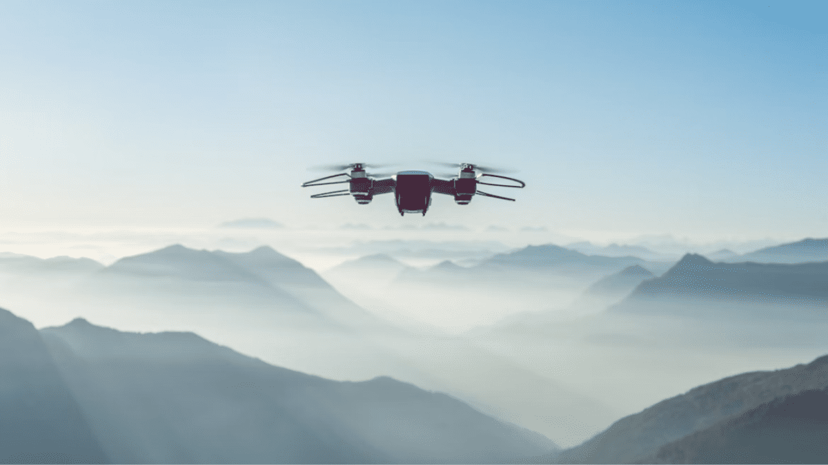 Dron letí nad hmlistými horami v pozadí modrej oblohy.