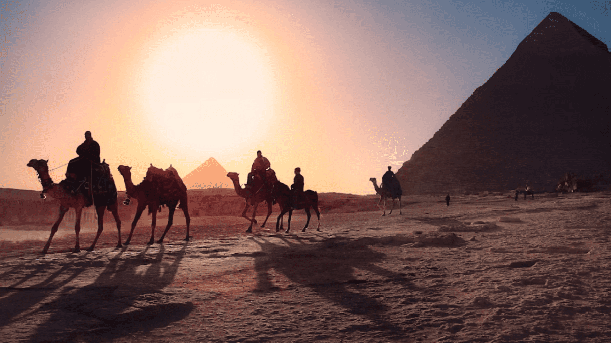 Jazda na ťavách pri pyramídach v Egypte počas západu slnka.