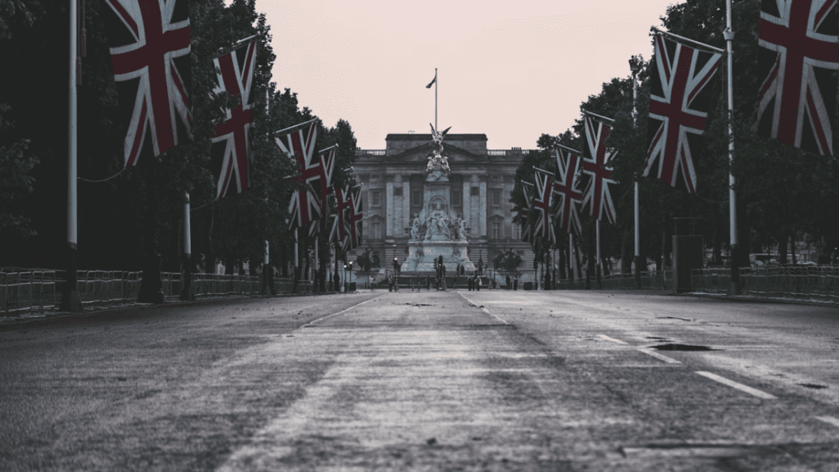 Cesta s britskými vlajkami vedúca k historickej budove za úsvitu, obloha jemne oranžová.
