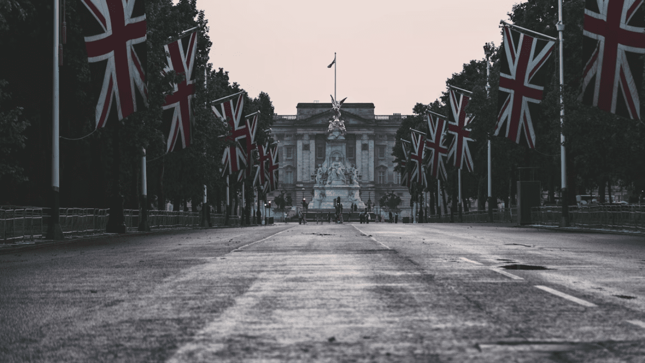 Cesta s britskými vlajkami vedúca k historickej budove za úsvitu, obloha jemne oranžová.