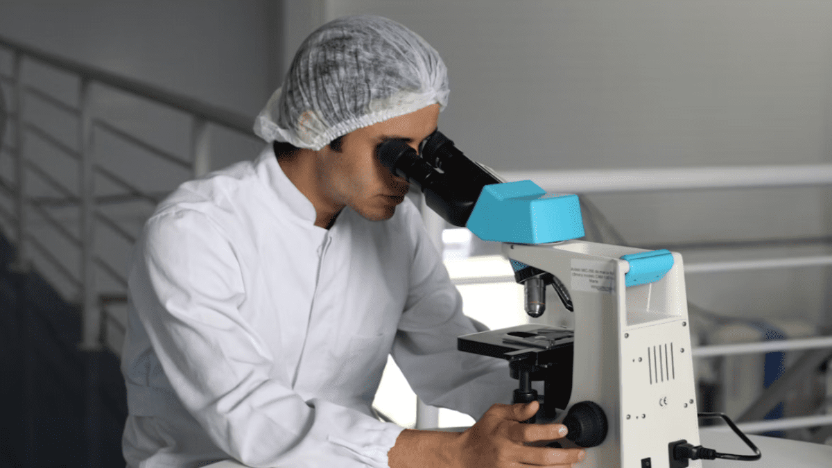 Vedec v bielom pracovnom plášti skúma vzorku pod mikroskopom v laboratóriu.