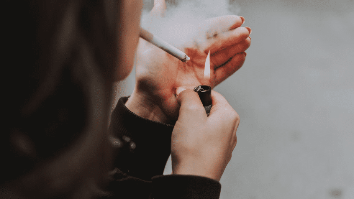 Osoba si zapaľuje cigaretu zapaľovačom, ruky si chráni pred vetrom.