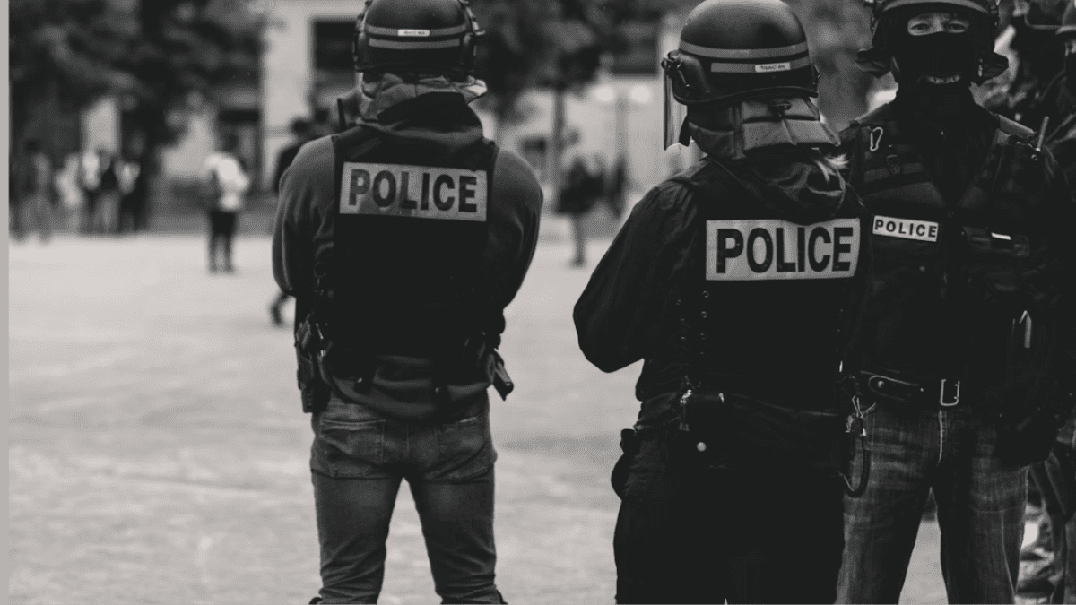 Policajti v taktickom vybavení na námestí, čiernobiela fotografia mestského prostredia so zameraním na bezpečnosť.