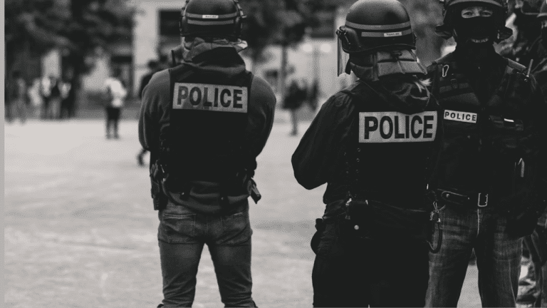 Policajti v taktickom vybavení na námestí, čiernobiela fotografia mestského prostredia so zameraním na bezpečnosť.
