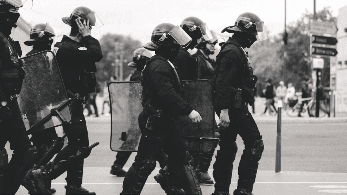 Policajti v zásahovej výstroji so štítmi kráčajú po ulici počas verejnej demonstrácie.