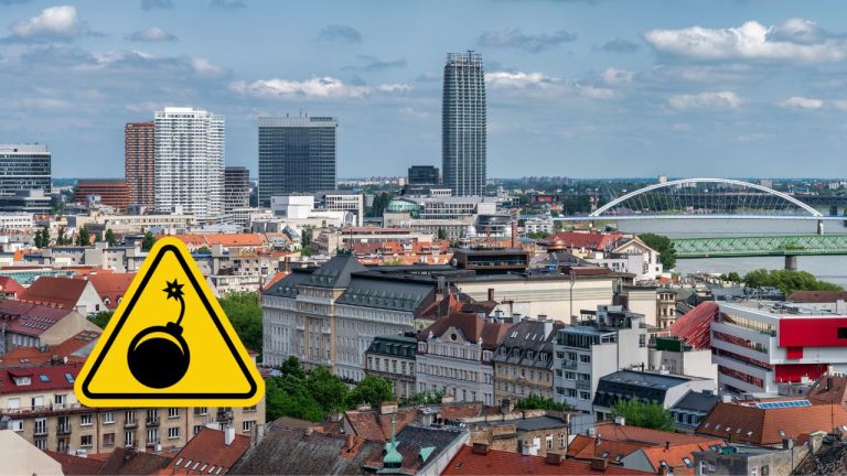 Panoráma mesta s výstražným symbolom bomby na popredí.
