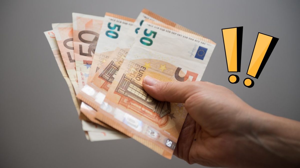 Osoba držiaca eurá v ruke s výraznými žltými výkričníkmi na sivom pozadí.