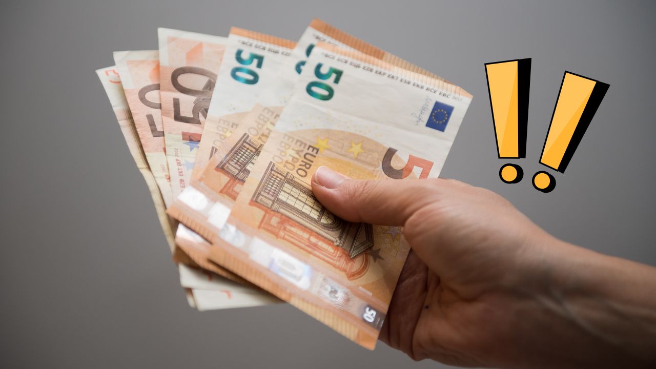 Osoba držiaca eurá v ruke s výraznými žltými výkričníkmi na sivom pozadí.