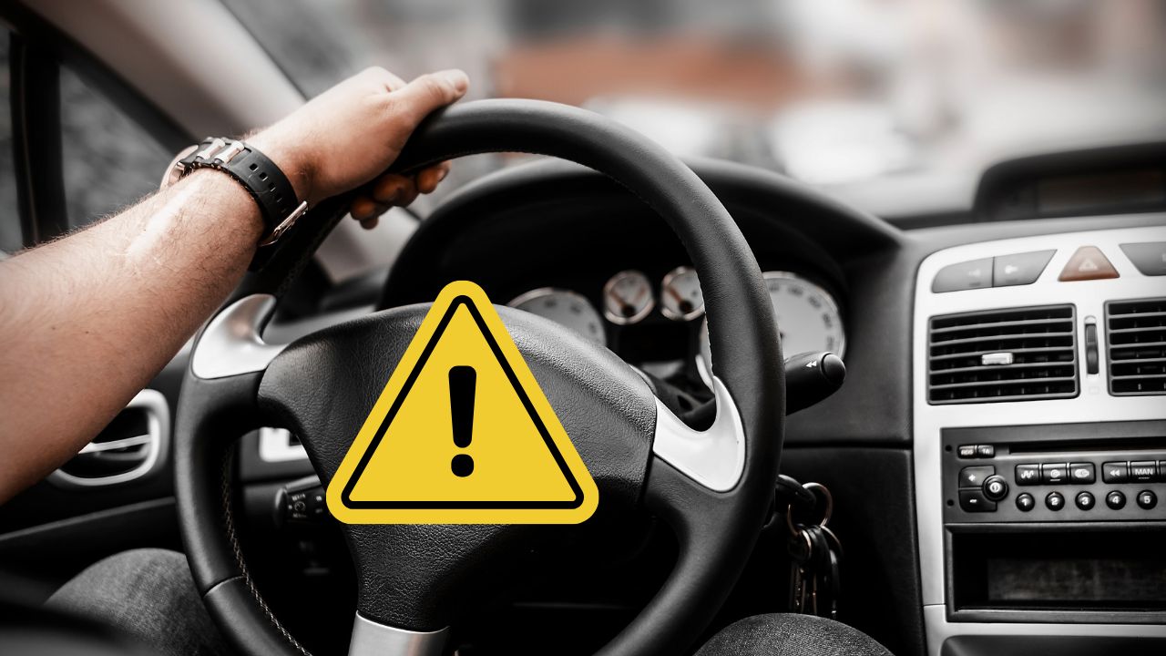 Ruka na volante auta s upozornením na bezpečnosť jazdy a žltým výstražným symbolom.