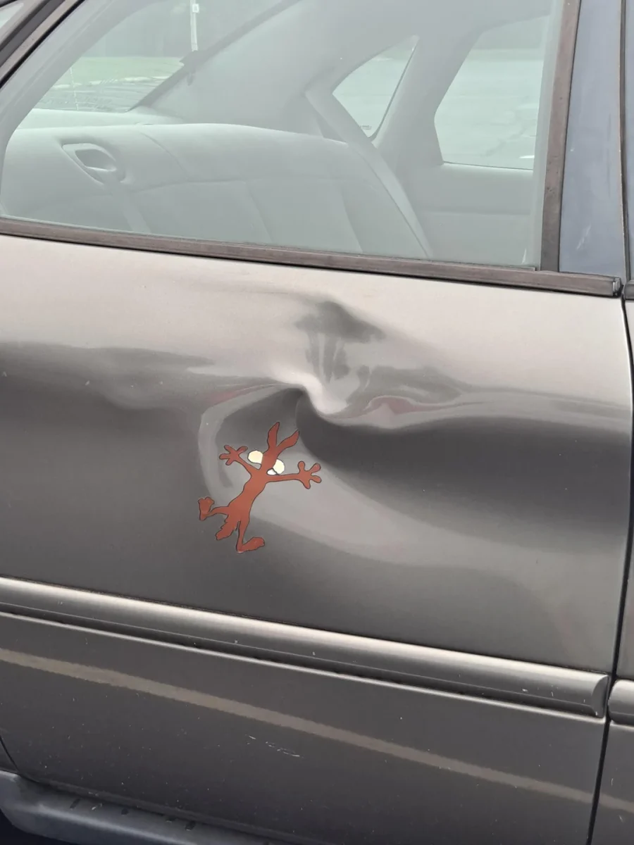 Auto s preliačinou na dverách ozdobené nálepkou kresleného vlka, vtipný nádych na opravu poškodenia.