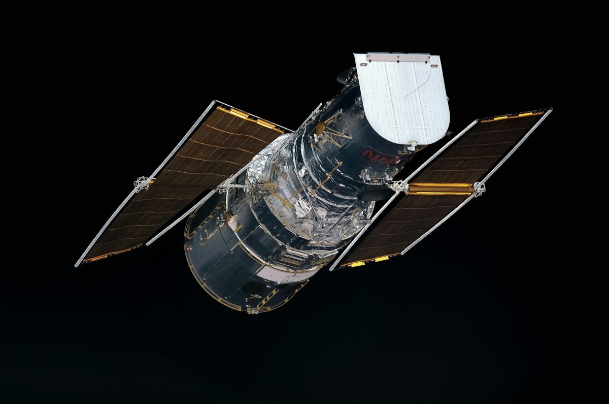 Hubblov teleskop vo vesmíre s rozvinutými solárnymi panelmi proti čiernej oblohe.