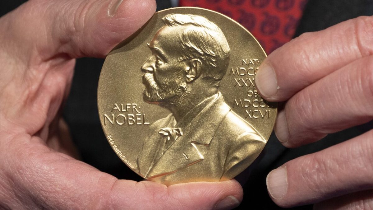 Osoba držiaca zlatú medailu s reliéfom muža, s nápisom Alfr. Nobel, symbolizujúca prestížne ocenenie.
