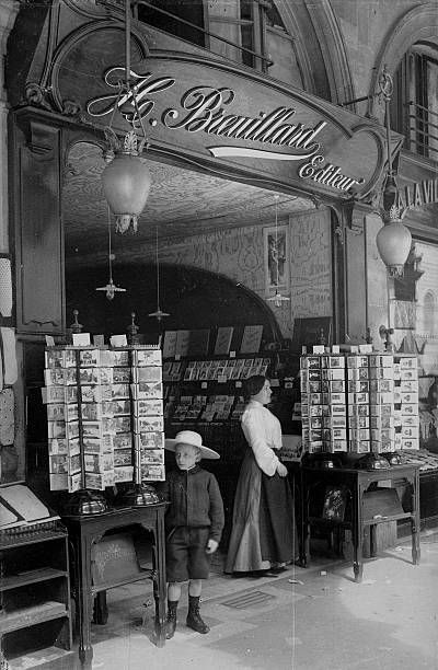 Historická kníhkupectvo s pohľadnicami, pred ktorým stojí žena a dieťa v klobúkoch.