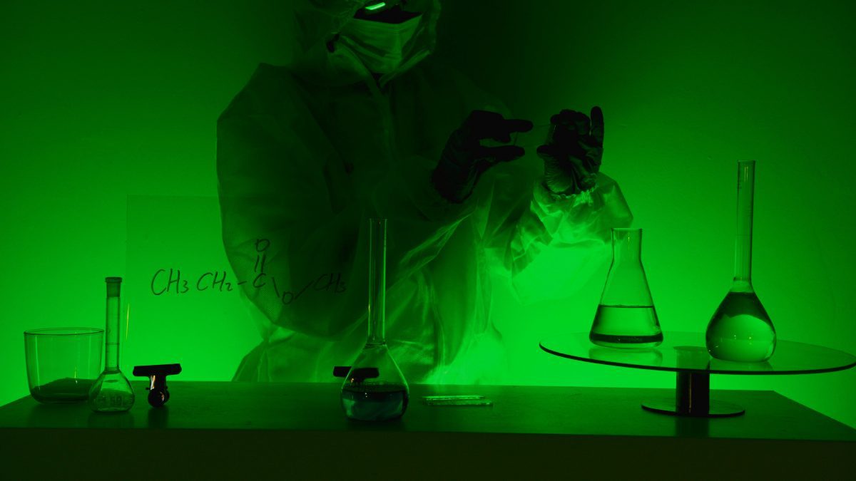 Vedec v ochrannom obleku pracuje v laboratóriu so skúmavkami pod zeleným svetlom.