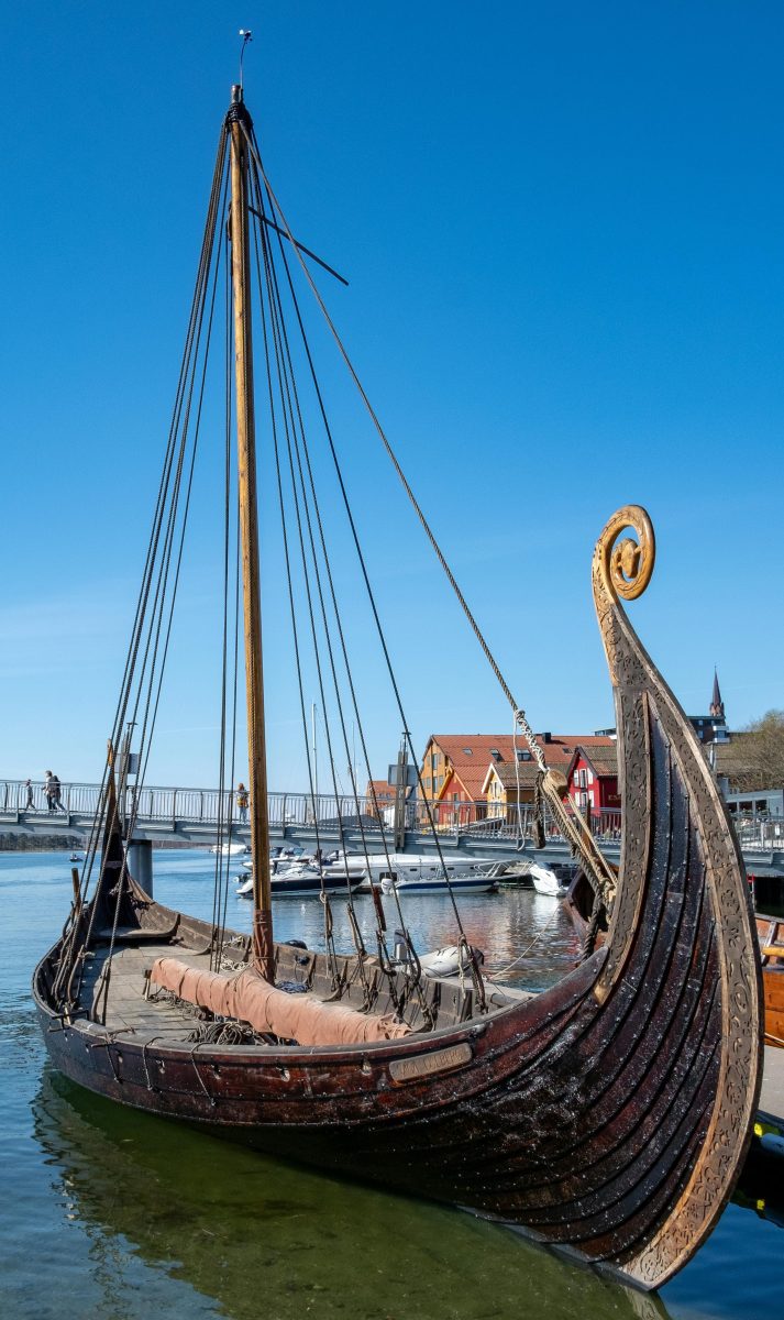 Starodávna vikingská drevená loď kotví v prístave pod modrou oblohou.