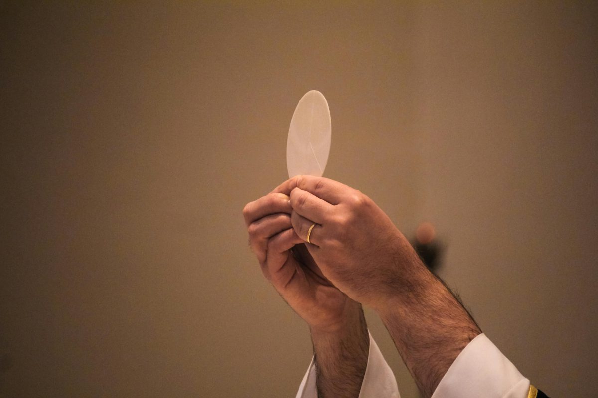 Kňaz drží hostiu pri katolíckej omši. Detailný záber rúk počas liturgického obradu.