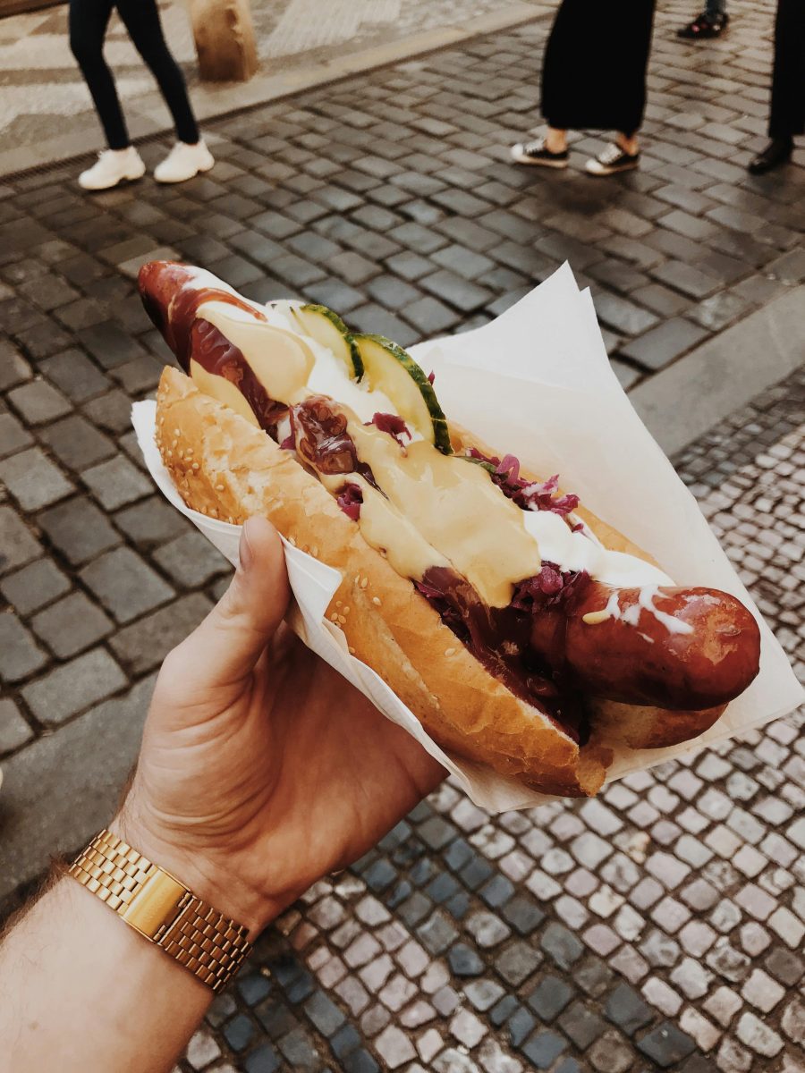 Chutný hotdog s klobásou, cibuľou a omáčkami na dláždenej ulici, ideálne rýchle jedlo na cestách.