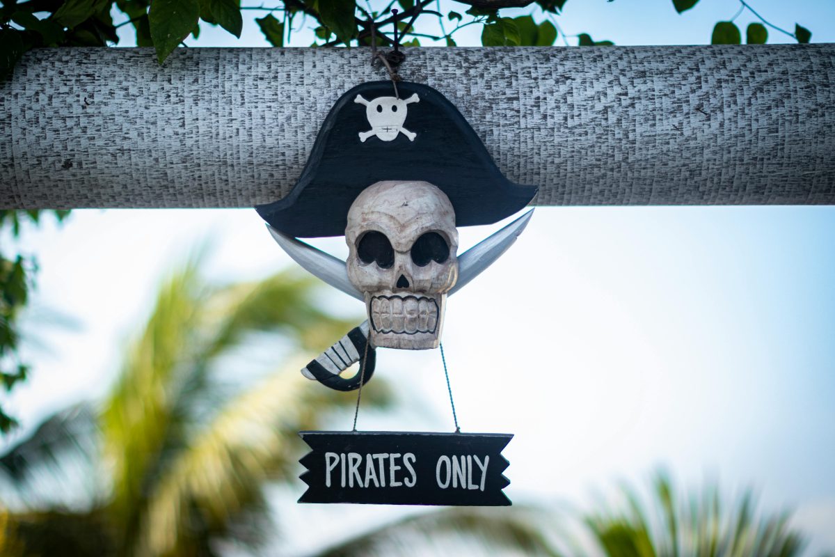 Pirátska dekorácia s lebkou a nápisom Pirates Only ozdobuje drevenú konštrukciu medzi listami v pozadí.