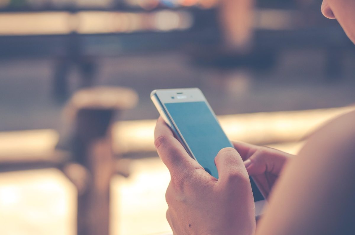 Osoba držiaca smartphone vonku, sústredená na obrazovku pod jemným slnečným svetlom.