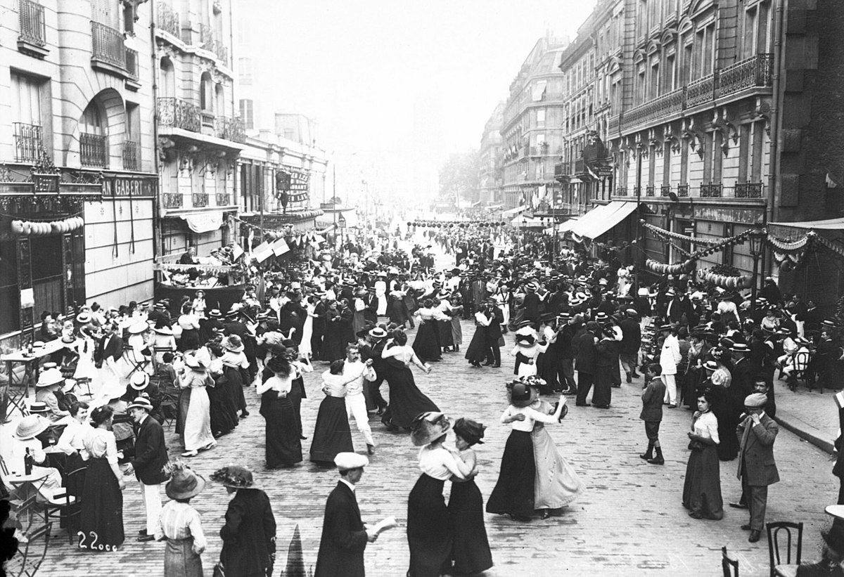 Historická ulica plná tancujúcich ľudí počas oslavy, mestská scéna s budovami a dekoráciami.