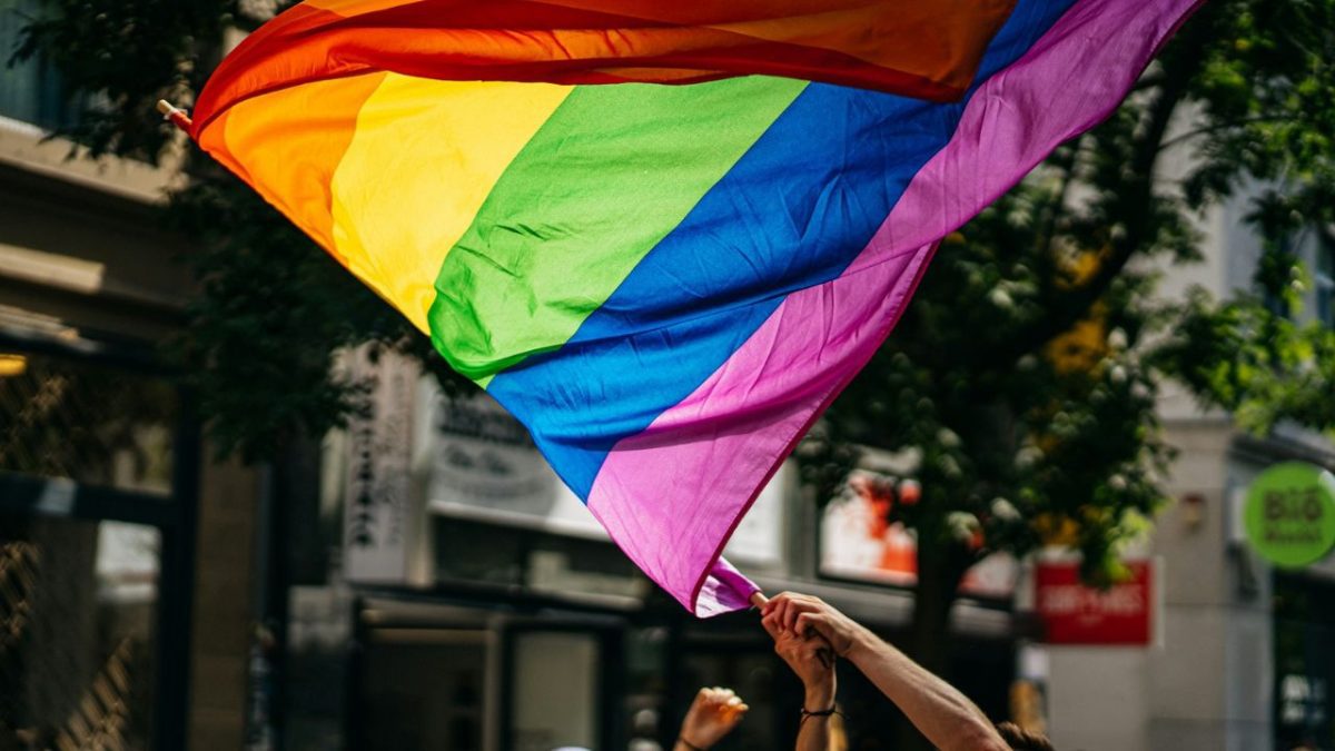 Dúhová vlajka v rukách ľudí na ulici počas slnečného dňa, symbol LGBT komunity a práv.