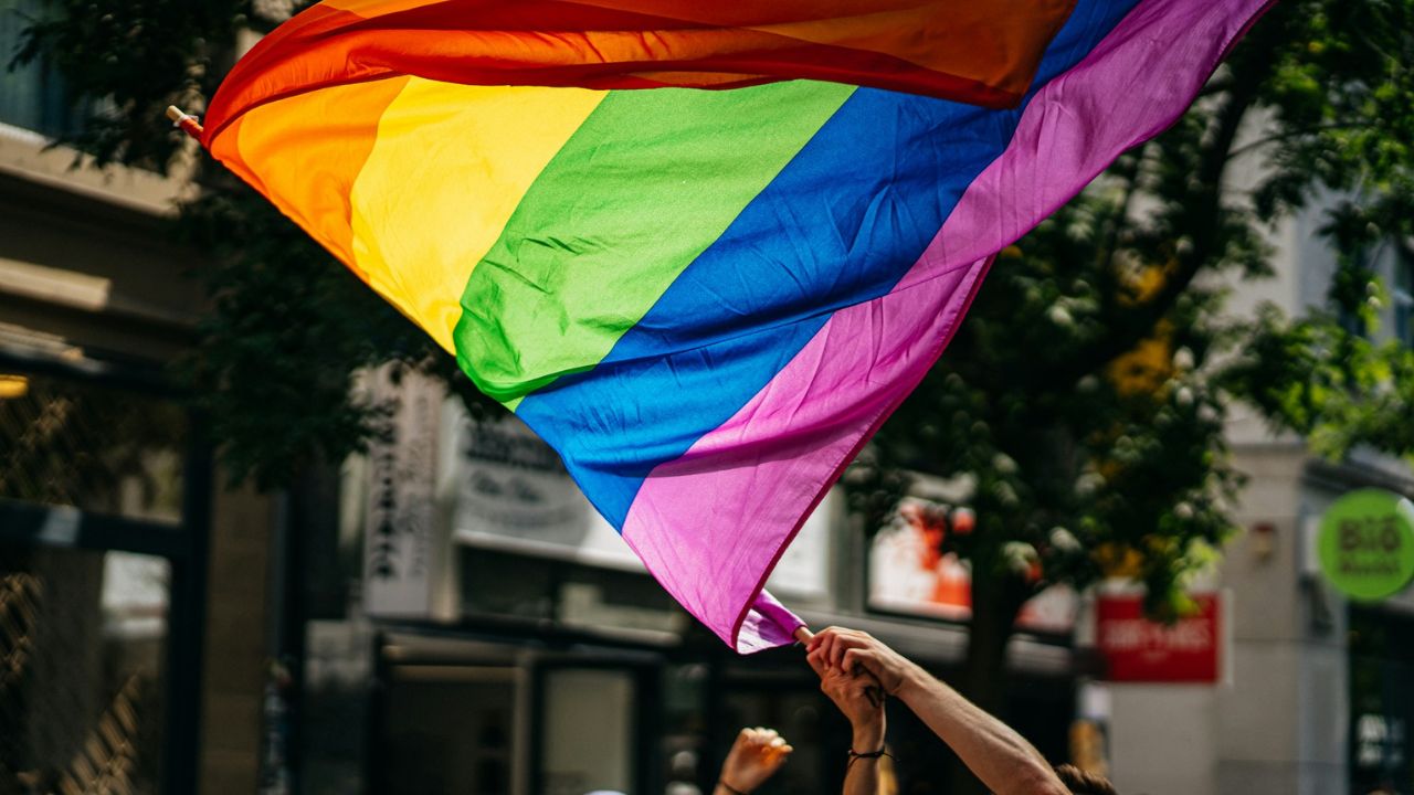 Dúhová vlajka v rukách ľudí na ulici počas slnečného dňa, symbol LGBT komunity a práv.