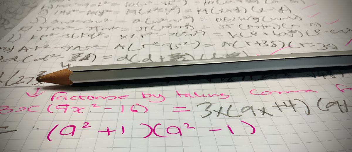 Písané matematické výpočty na mriežkovanom papieri s ceruzkou položenou na vrchu.