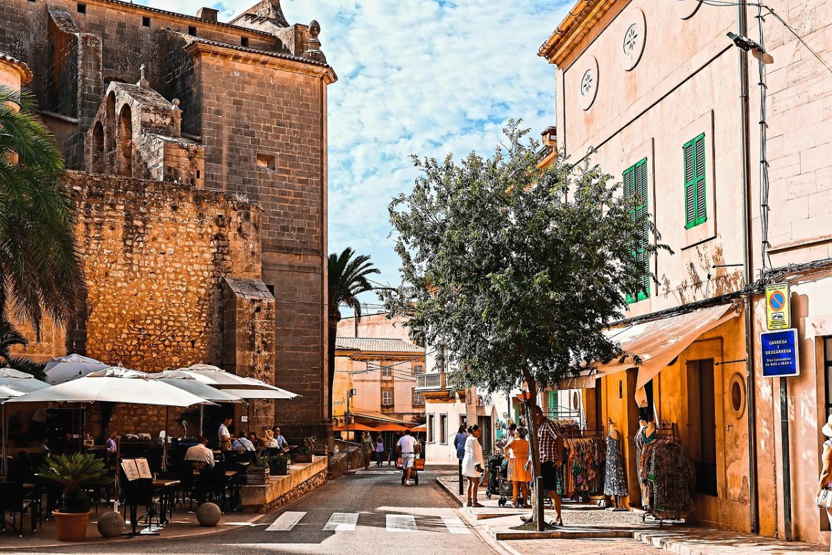 Malebná ulička s historickou architektúrou, kaviarňou a obchodíkmi na slnečnom námestí.