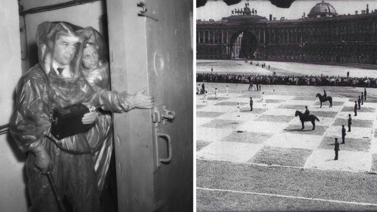 Ľudia v ochranných oblekoch a veľká vonkajšia šachovnica s hráčmi v historických uniformách na námestí.