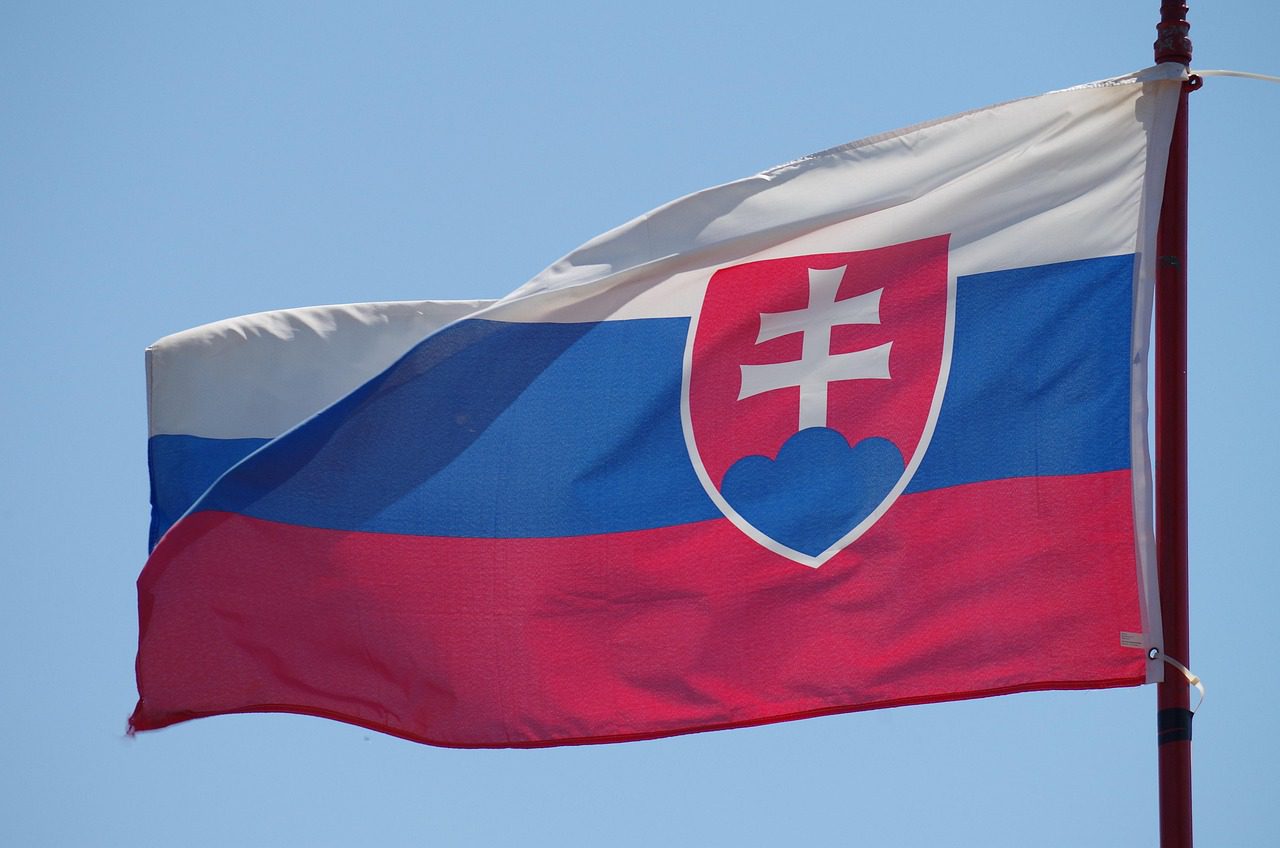 Slovenská vlajka vejúca vo vetre na modrom pozadí, štátny symbol Slovenskej republiky.