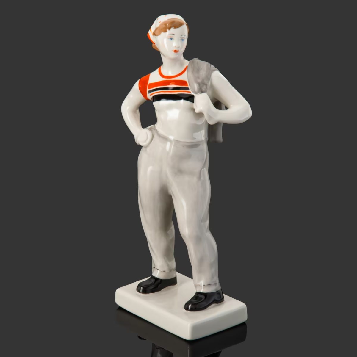 Porcelánová soška námorníka v pruhovanom tričku s rukou na boku na tmavom pozadí.