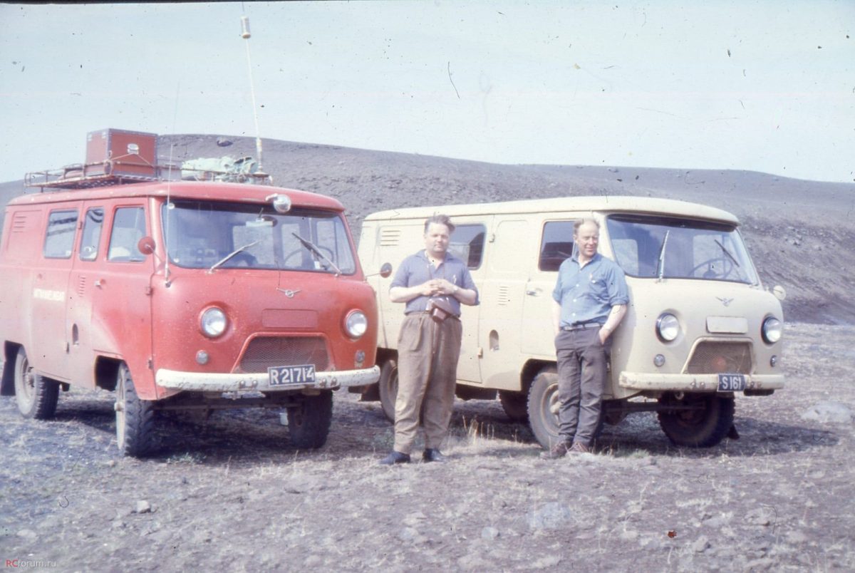 Dvaja muži stoja pred červeným a béžovým retro mikrobusom na kamenistom teréne.