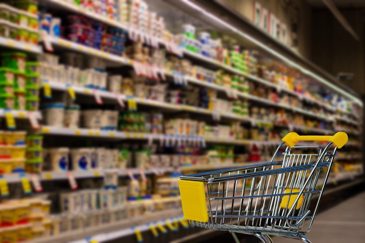 Nákupný vozík v uličke s potravinami plnej rôznych produktov v supermarkete.