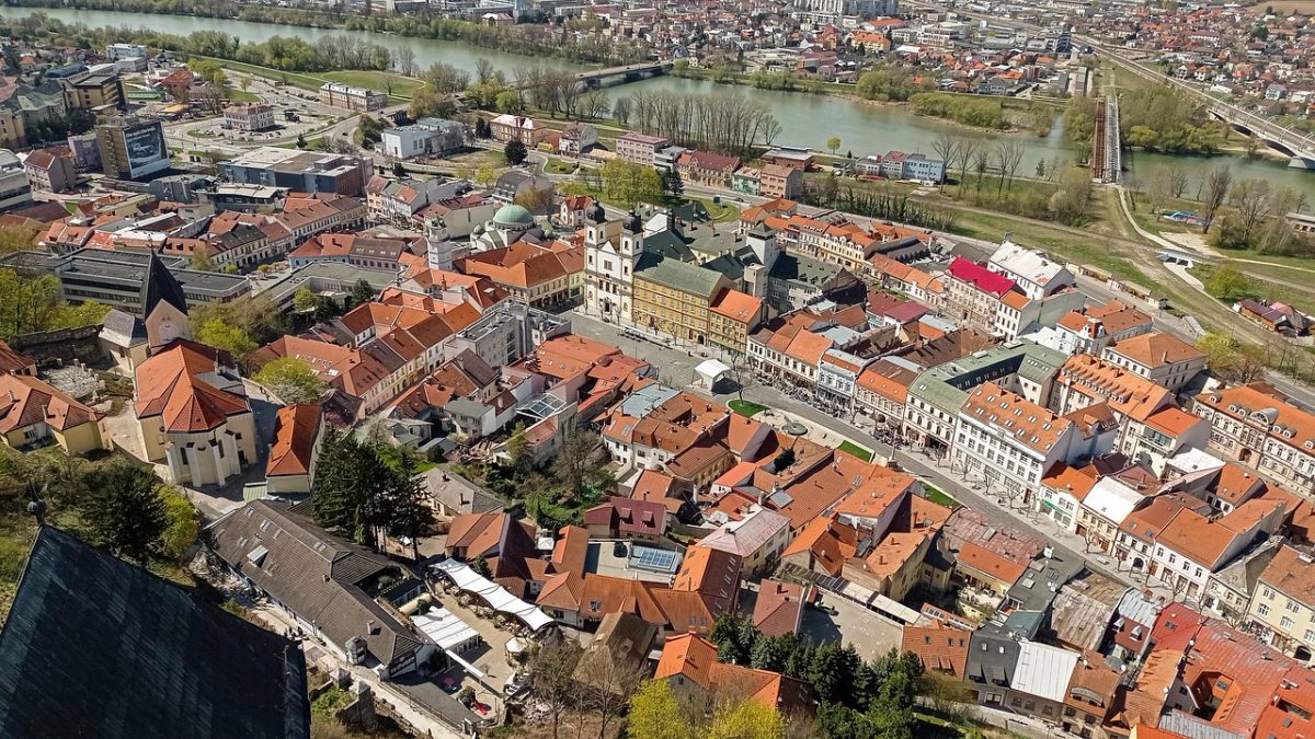 Pohľad z výšky na historické centrum mesta s riekou a mostom v pozadí na slnečný deň.