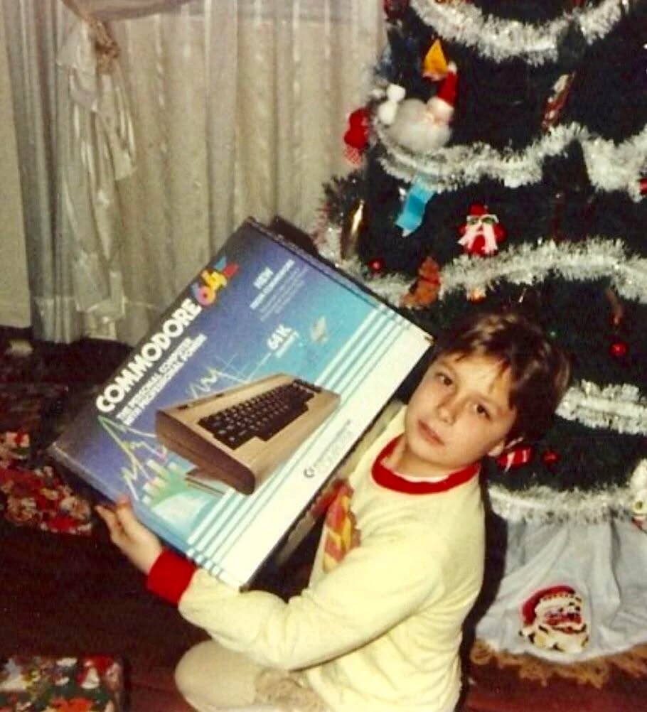 Chlapec drží darčekovú krabicu s počítačom Commodore 64 pred vianočným stromčekom.