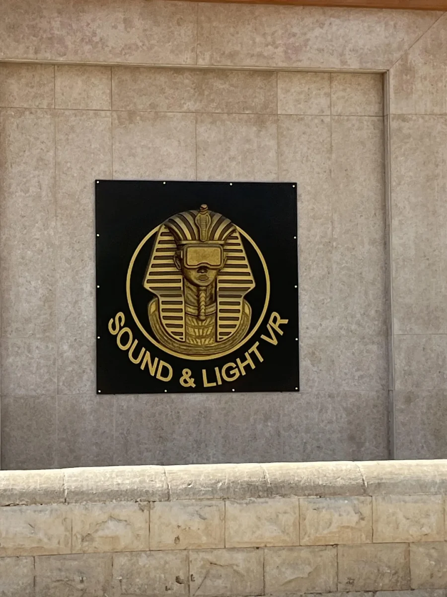 Zlatý znak Sound & Light VR s faraónom s VR okuliarmi na kamennej stene.