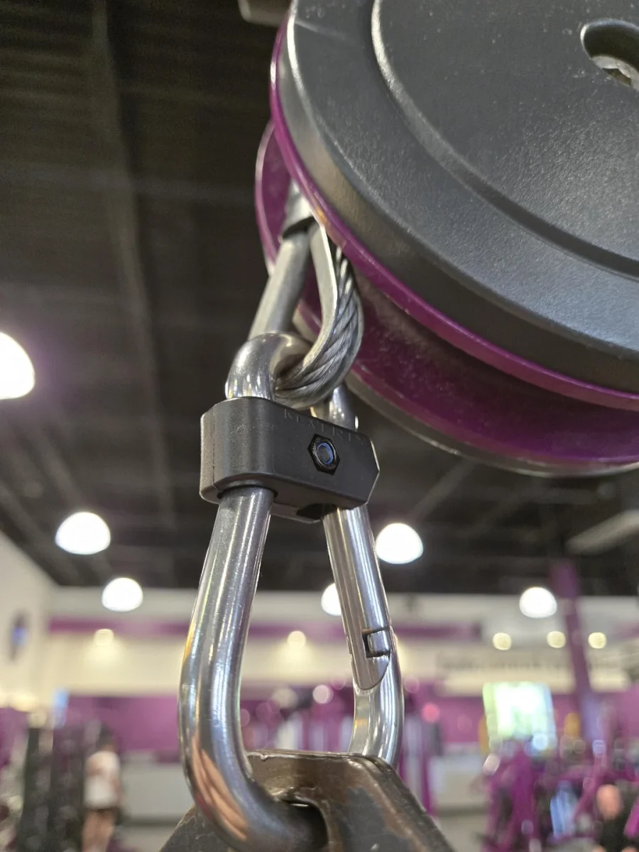 Záber na karabínu s oceľovým lanom v posilňovni, detail na zariadenie fitness stroja.