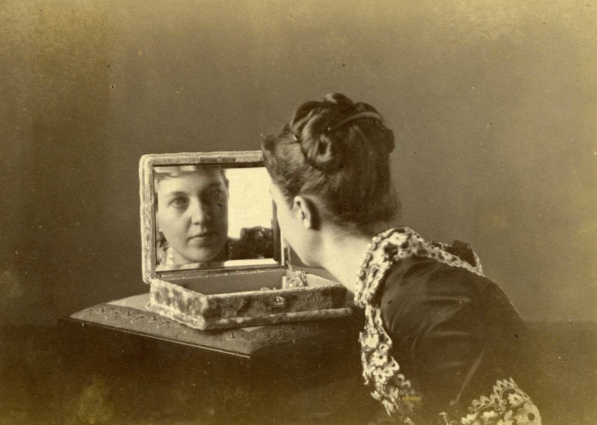 Žena s vyčesanými vlasmi sa pozerá do zrkadla starožitnej šperkovnice. Vintage fotografia.