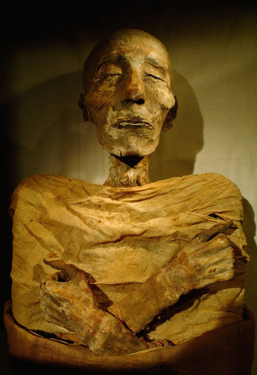 Staroveká egyptská múmia s prekříženými rukami a zatvorenými očami, obalená v látke.