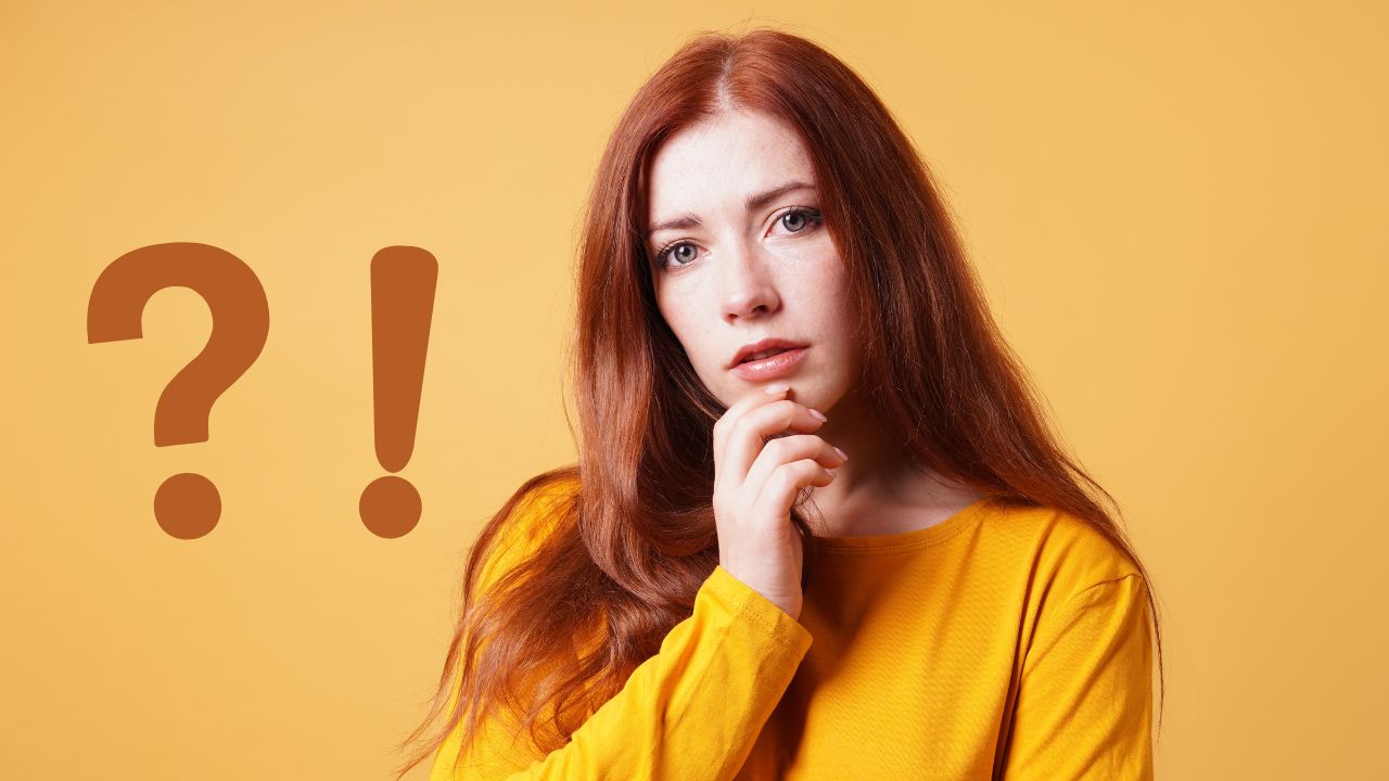 Žena v žltom tričku s otáznikom a výkričníkom na oranžovom pozadí premýšľa.