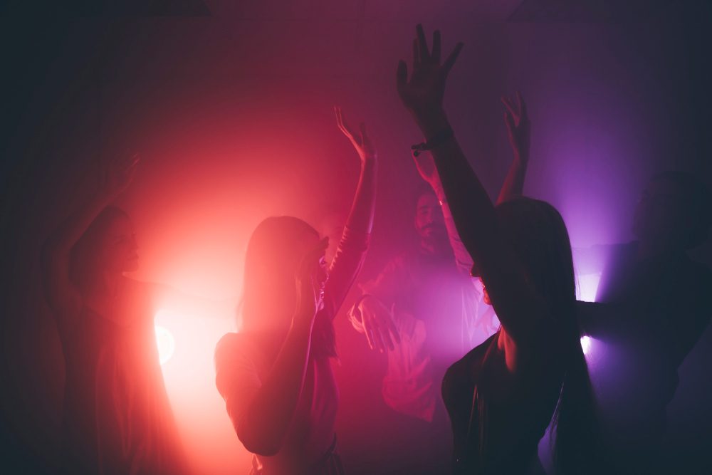 Ľudia tancujú na party s farebnými svetlami, veselá atmosféra plná energie.